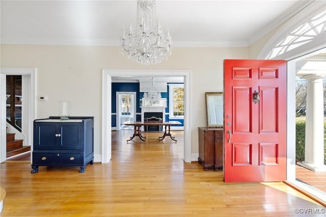 entrance foyer featuring light wood-style floors, a fireplace, ornamental molding, and a notable chandelier