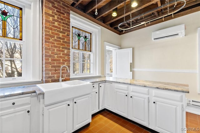 kitchen featuring light stone counters, white cabinets, a wall mounted air conditioner, and a sink