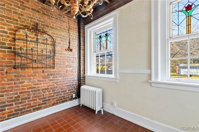 spare room with brick wall, radiator heating unit, and baseboards