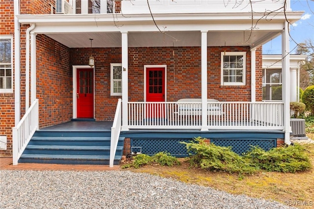 entrance to property with covered porch, brick siding, and cooling unit