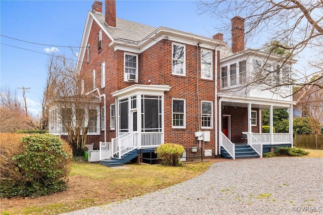 view of front of property with covered porch, brick siding, a chimney, and a sunroom