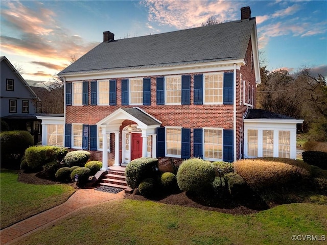 view of front of home with a chimney, a lawn, and brick siding