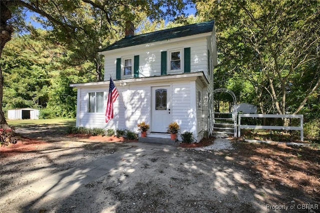 view of front of home with driveway, a chimney, and fence