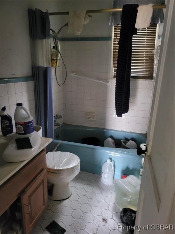 bathroom featuring toilet, vanity, tile walls, wainscoting, and shower / bath combination with curtain