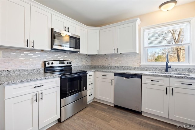 kitchen featuring a sink, stainless steel appliances, light wood-type flooring, white cabinetry, and backsplash