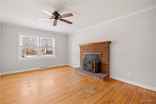 unfurnished living room featuring a wood stove, light wood-style flooring, visible vents, and crown molding