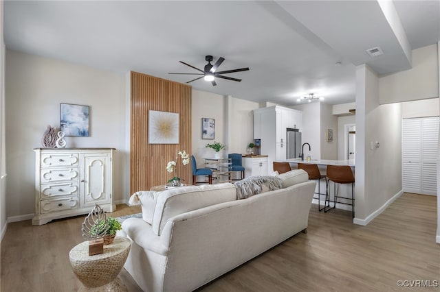 living room featuring light wood finished floors, baseboards, visible vents, and a ceiling fan