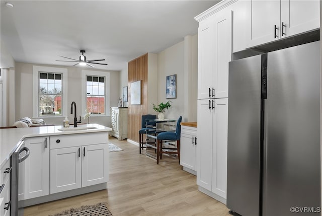 kitchen featuring stainless steel appliances, a sink, white cabinetry, light countertops, and light wood finished floors