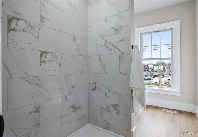 full bath with visible vents, tiled shower, baseboards, and wood finished floors