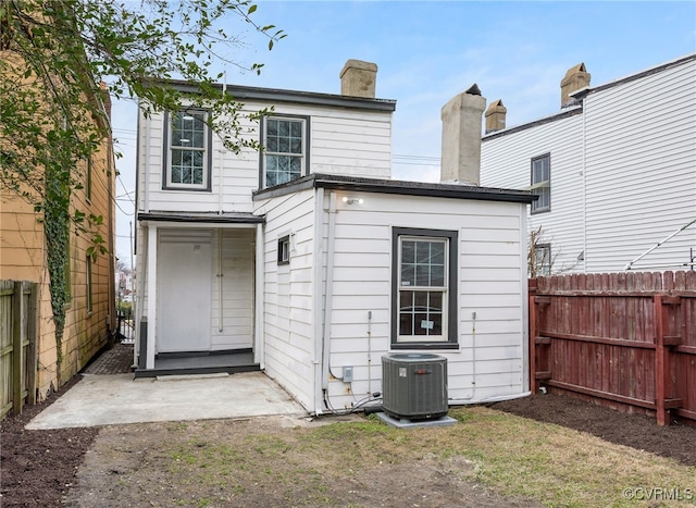 back of house with central air condition unit, a chimney, and fence