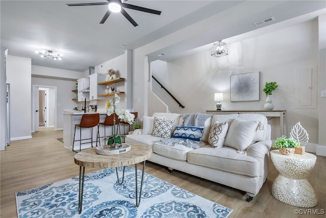 living area featuring ceiling fan with notable chandelier, light wood finished floors, visible vents, and baseboards