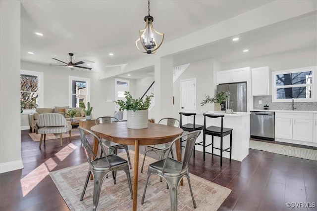 dining room with ceiling fan with notable chandelier, baseboards, dark wood-style flooring, and recessed lighting