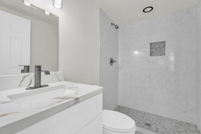 bathroom featuring toilet, tiled shower, and vanity