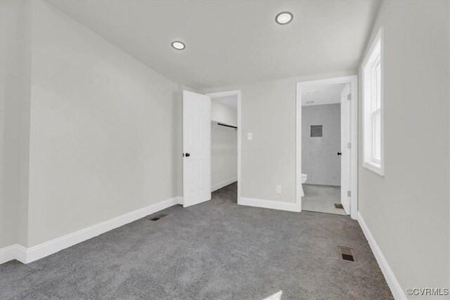 unfurnished bedroom featuring connected bathroom, visible vents, baseboards, dark carpet, and a walk in closet