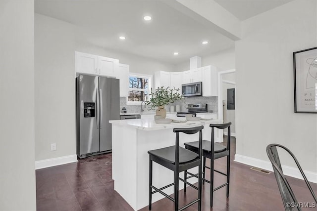 kitchen with decorative backsplash, appliances with stainless steel finishes, a breakfast bar area, light countertops, and white cabinetry