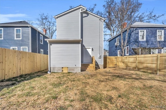 back of house with entry steps, a fenced backyard, and a lawn