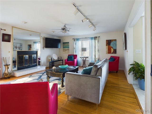 living area with light wood finished floors, ceiling fan, a tiled fireplace, and rail lighting