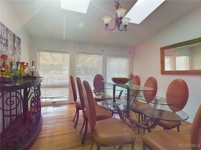 dining area with light wood-type flooring, vaulted ceiling with skylight, and a chandelier