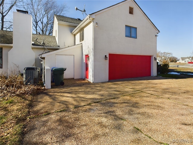 view of side of home with a chimney, stucco siding, an attached garage, central AC unit, and driveway