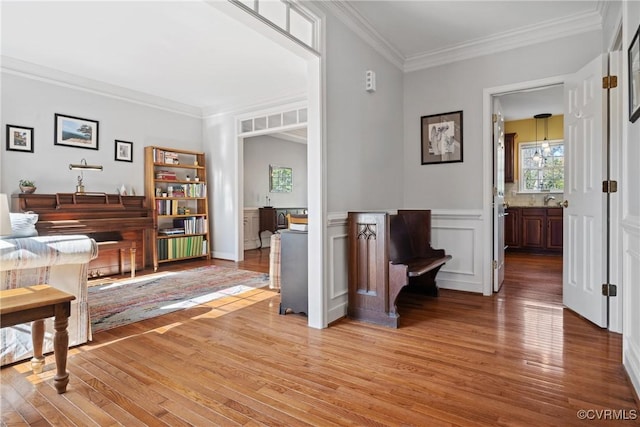 living area featuring light wood-type flooring, a wainscoted wall, and ornamental molding