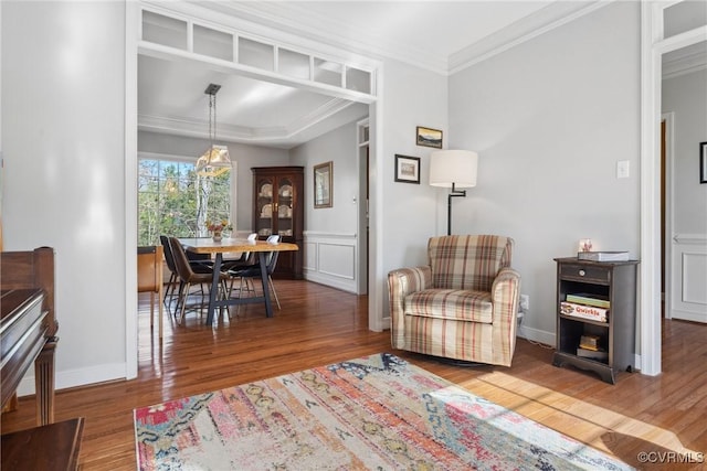 living area with a decorative wall, wood finished floors, baseboards, and ornamental molding