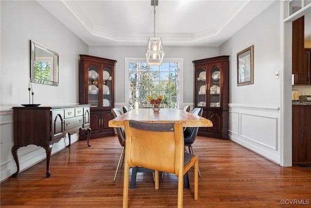 dining space featuring a wainscoted wall, a tray ceiling, wood finished floors, crown molding, and a decorative wall