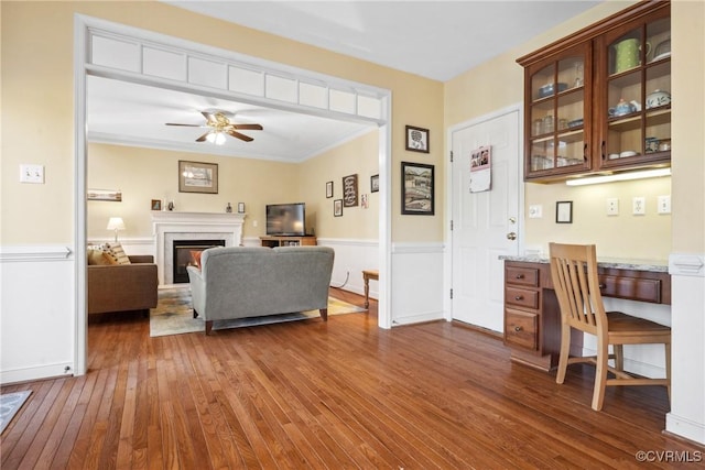 interior space featuring a glass covered fireplace, ornamental molding, ceiling fan, and dark wood-style flooring