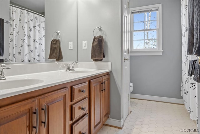 bathroom with a sink, baseboards, toilet, and double vanity