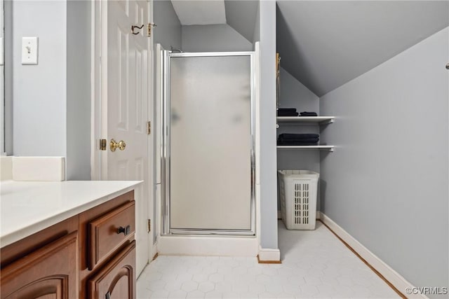 bathroom with a stall shower, vanity, baseboards, and vaulted ceiling