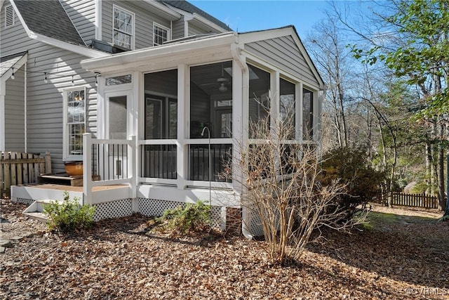 view of home's exterior featuring a sunroom, fence, and roof with shingles