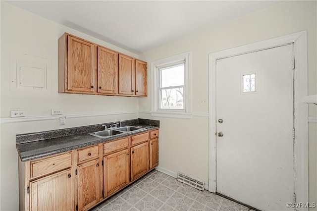 kitchen featuring baseboards, visible vents, brown cabinetry, dark countertops, and a sink