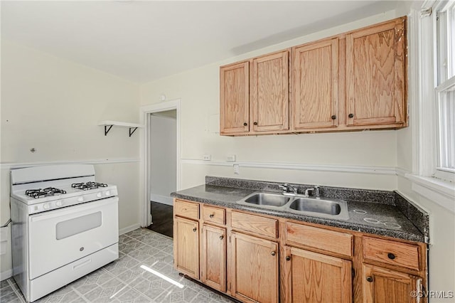 kitchen with dark countertops, light brown cabinets, a sink, and gas range gas stove