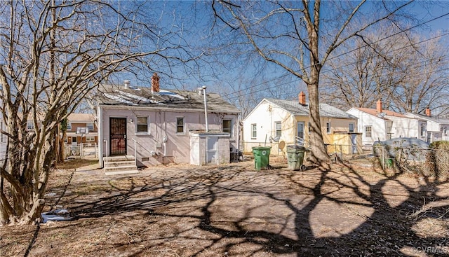 back of house featuring entry steps, a chimney, fence, and a residential view