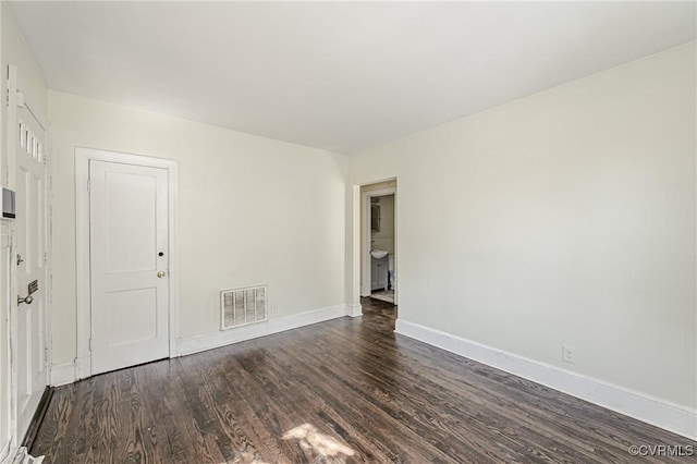 empty room featuring baseboards, visible vents, and dark wood-style flooring