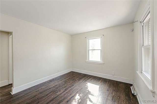 spare room featuring a baseboard heating unit, dark wood-style flooring, and baseboards