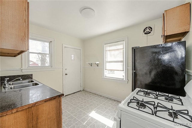 kitchen featuring white range with gas cooktop, dark countertops, freestanding refrigerator, light floors, and a sink