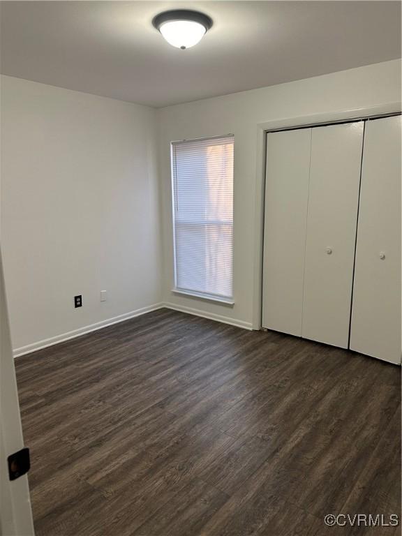 unfurnished bedroom featuring dark wood-style floors, a closet, and baseboards