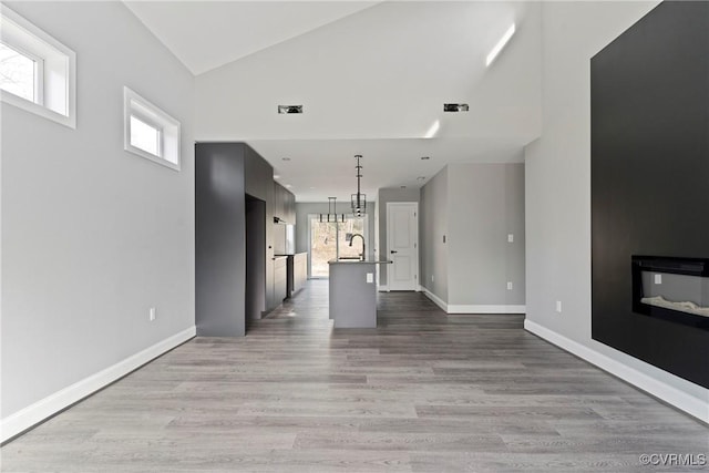 unfurnished living room with light wood finished floors, baseboards, vaulted ceiling, and a glass covered fireplace