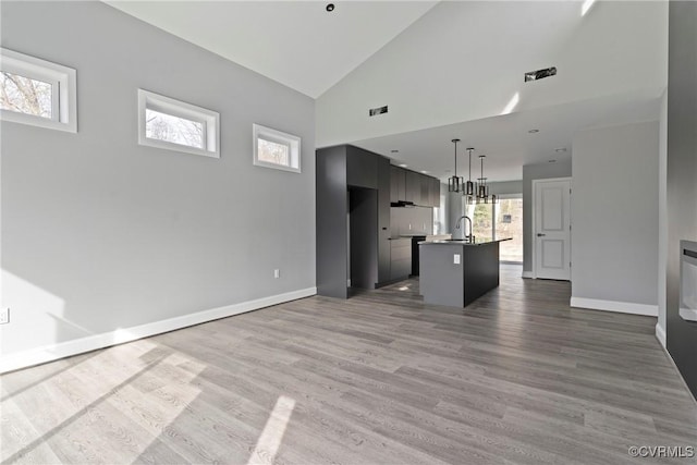 unfurnished living room featuring high vaulted ceiling, a sink, baseboards, and wood finished floors