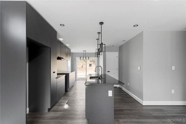 kitchen featuring dark wood-style floors, a kitchen island with sink, a sink, modern cabinets, and baseboards