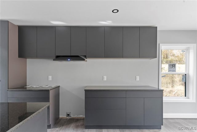 kitchen featuring light wood-type flooring, gray cabinets, range hood, dark stone countertops, and modern cabinets