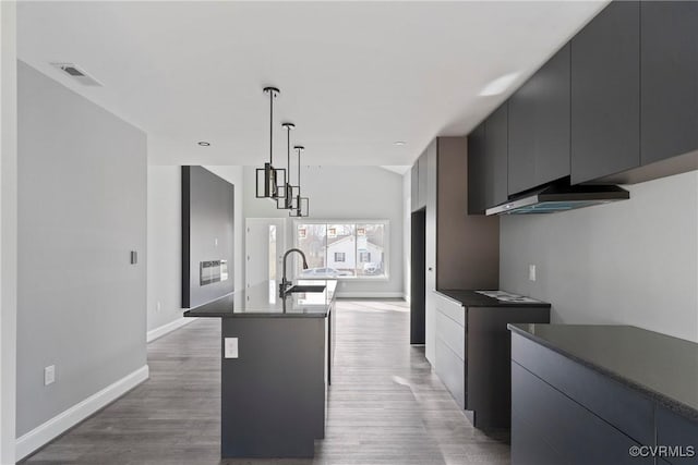 kitchen featuring a kitchen island with sink, a sink, hanging light fixtures, dark countertops, and modern cabinets