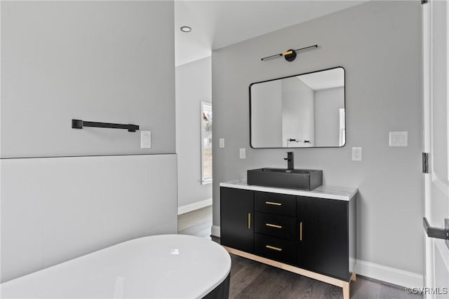 bathroom featuring wood finished floors, a freestanding tub, vanity, and baseboards