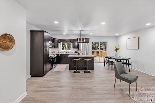 kitchen with a breakfast bar, hanging light fixtures, appliances with stainless steel finishes, a kitchen island, and a sink