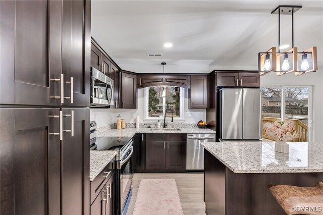 kitchen featuring visible vents, hanging light fixtures, appliances with stainless steel finishes, a sink, and light stone countertops