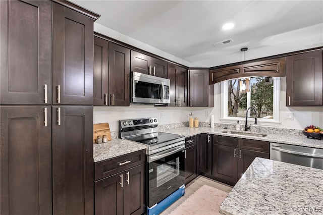 kitchen featuring appliances with stainless steel finishes, visible vents, a sink, and light stone countertops