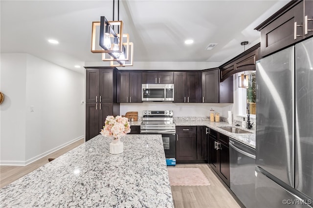 kitchen featuring dark brown cabinetry, visible vents, appliances with stainless steel finishes, light stone counters, and a sink