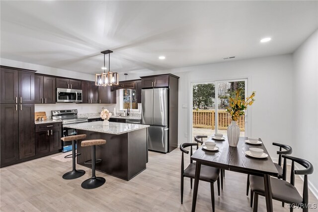 kitchen featuring stainless steel appliances, a kitchen island, hanging light fixtures, dark brown cabinets, and light wood finished floors