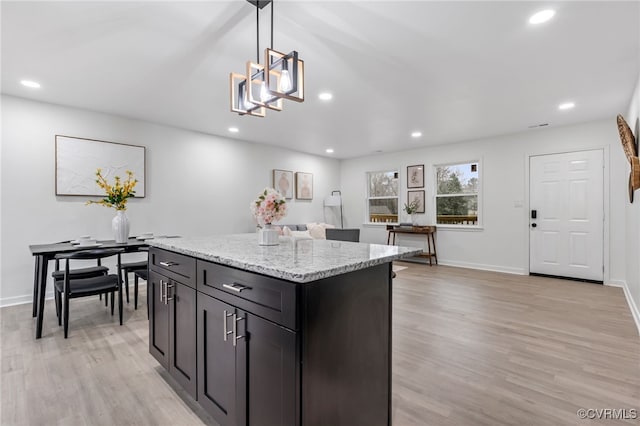 kitchen with light stone countertops, recessed lighting, hanging light fixtures, a center island, and light wood finished floors