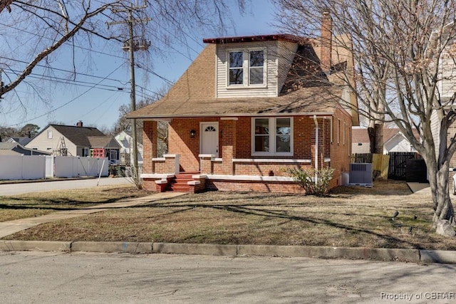 bungalow featuring brick siding, a front lawn, central AC unit, and fence